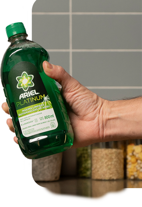 Una mano sostiene una botella plástica de 800 ml color verde de jabón líquido para la ropa Ariel Platinum máxima limpieza quitamanchas